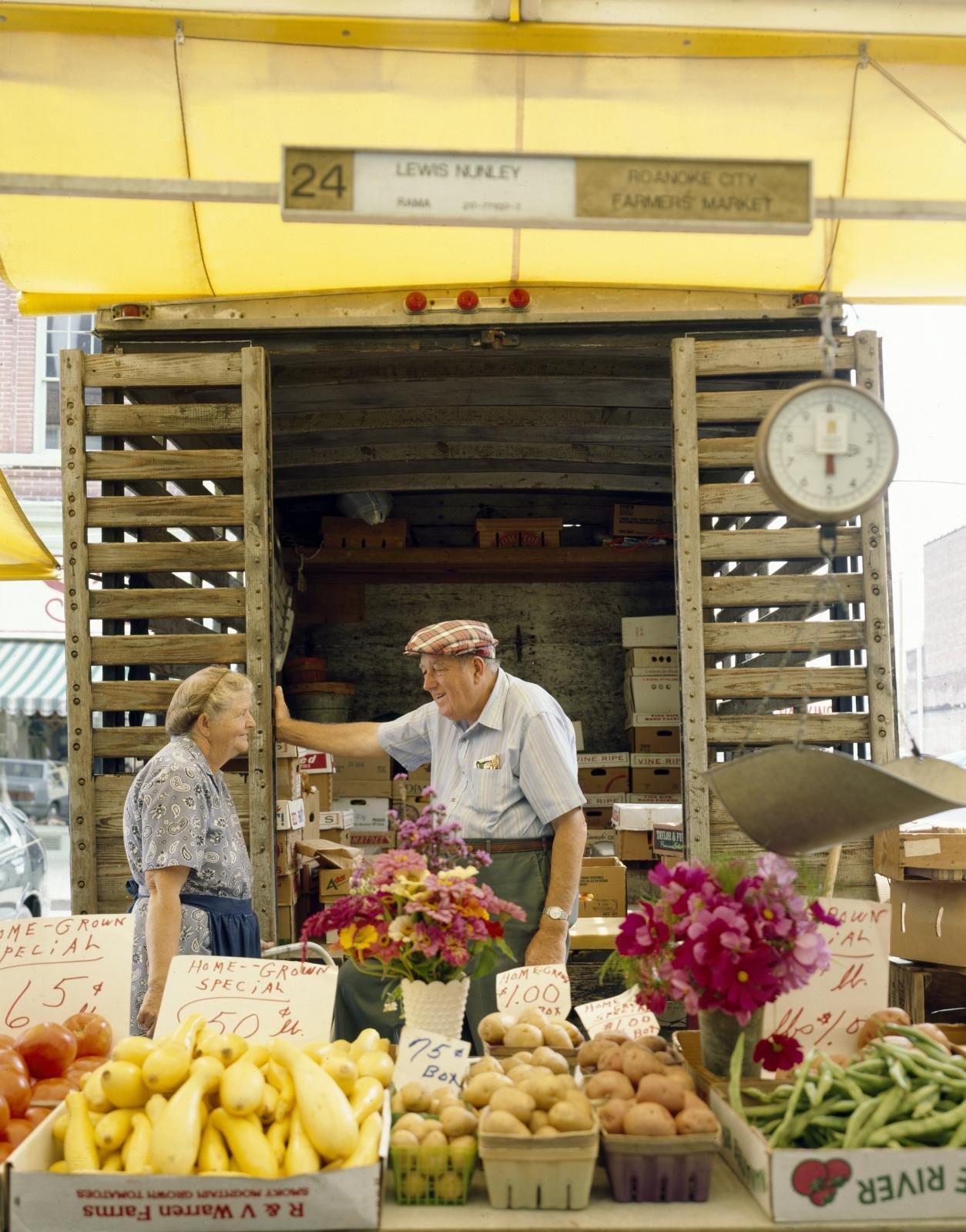 A farmers market stand stacked with fresh vegetables and cut flowers
